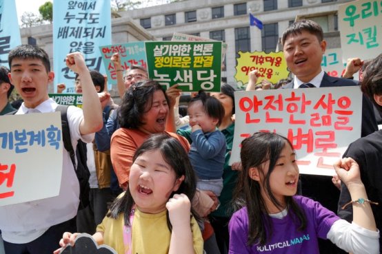 Environmental activists and plaintiffs, including children and a toddler, hold signs and chant slogans during a demonstration at the constitutional court in Seoul, South Korea.