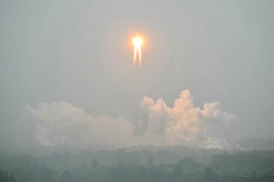 A firey orange ball hurtles over the clouds in a gray sky.